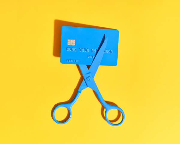 blue credit card about to be cut with blue scissors on a yellow background