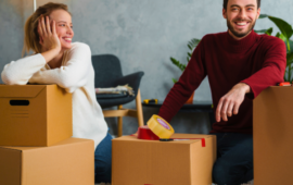 couple smiling wearing sweaters surrounded by boxes while preparing to move out