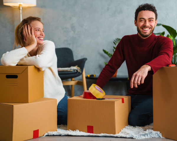 couple smiling wearing sweaters surrounded by boxes while preparing to move out