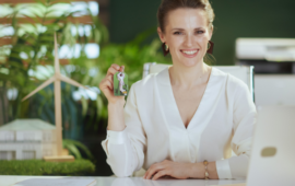 a female real estate agent working on her laptop smiling while holding out house keys