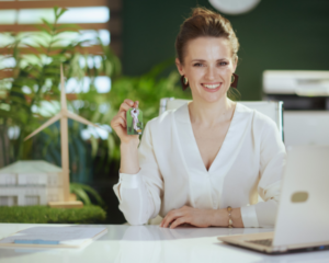 a female real estate agent working on her laptop smiling while holding out house keys