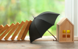 figurine of a home being protected by an umbrella from falling dominoes