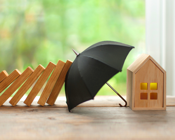 figurine of a home being protected by an umbrella from falling dominoes
