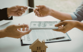 Two hands exchange cash and keys over a contract on a table, symbolizing a real estate transaction. A small house model is also visible in the foreground.