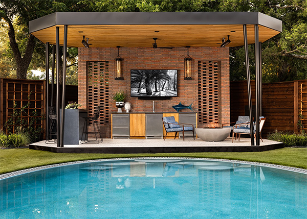 Modern patio with navy outdoor kitchen units on wheels, a black dog, and green tiled wall. Glass doors reveal an interior with orange chairs. Peaceful.