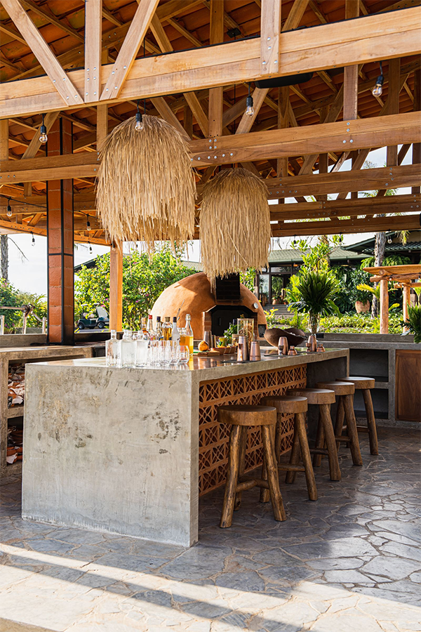 Modern patio with navy outdoor kitchen units on wheels, a black dog, and green tiled wall. Glass doors reveal an interior with orange chairs. Peaceful.