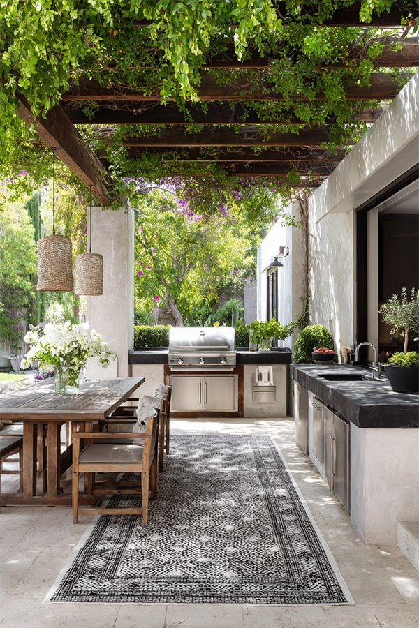 Modern patio with navy outdoor kitchen units on wheels, a black dog, and green tiled wall. Glass doors reveal an interior with orange chairs. Peaceful.