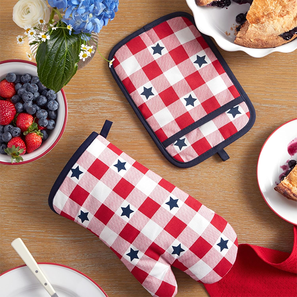 Red and white checkered oven mitt and pot holder with blue stars on a wooden table. Nearby, a bowl of berries, flowers, and a pie slice create a cozy, festive feel. Red and white checkered oven mitt and pot holder with blue stars on a wooden table. Nearby, a bowl of berries, flowers, and a pie slice create a cozy, festive feel.