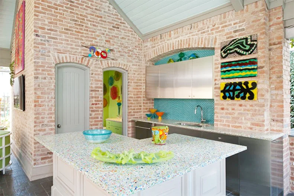 Modern patio with navy outdoor kitchen units on wheels, a black dog, and green tiled wall. Glass doors reveal an interior with orange chairs. Peaceful.