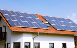 White house with a terracotta roof covered in blue solar panels beneath a clear sky, conveying clean energy and sustainable living.