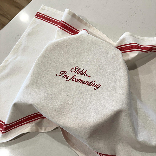 Two folded plaid linen towels embroidered resting on a dark patterned rug beside wooden frames