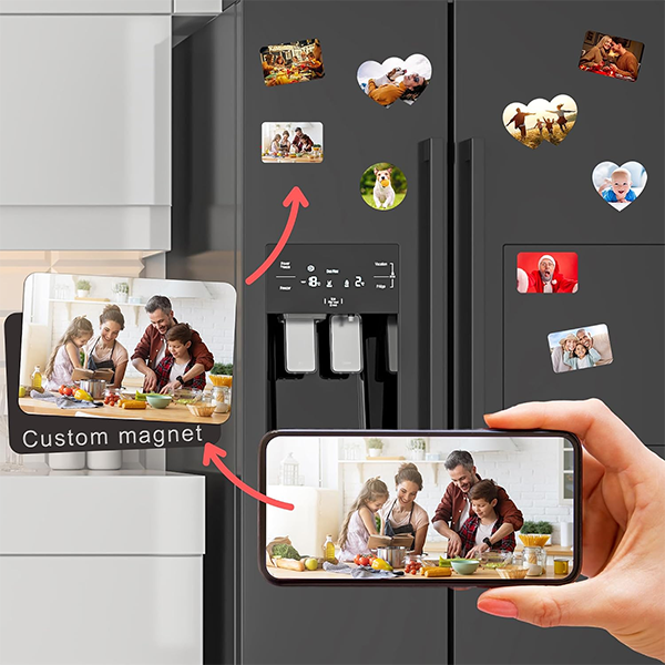 Custom photo magnets decorate a dark refrigerator, showing a smiling family cooking; a hand holds a phone displaying the same family photo.