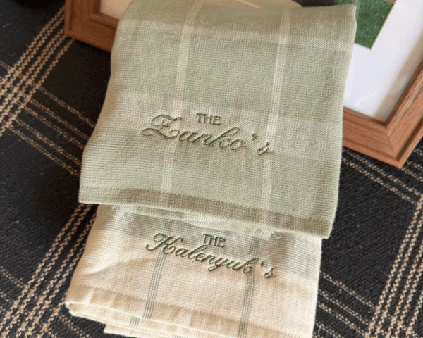 Two folded plaid linen towels embroidered resting on a dark patterned rug beside wooden frames